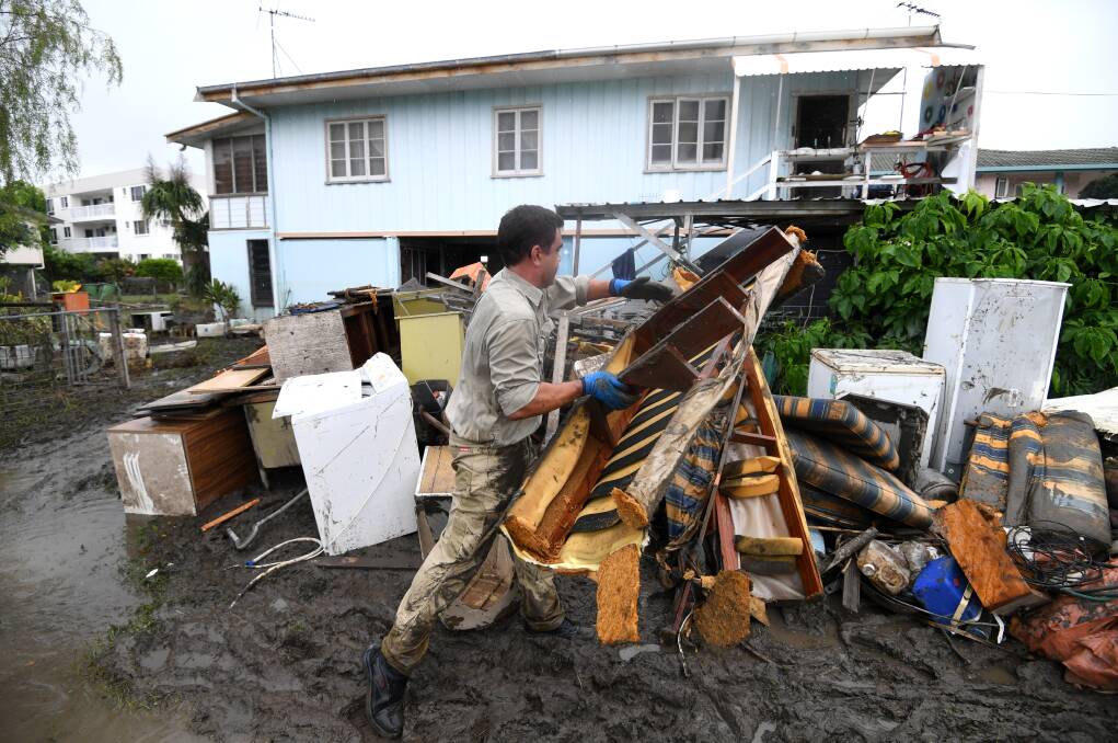 A man helps strangers remove flood-damaged items from their home in the suburb of Rosslea in Townsville on Thursday.  Photo: AAP Image/ Dan Peled