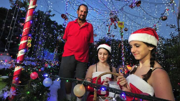 Phil Jensen in his Kambah Christmas lights display with his granddaughters Chelsea Scarcella,11 and Maddison Scarcella,13. Photo: Melissa Adams