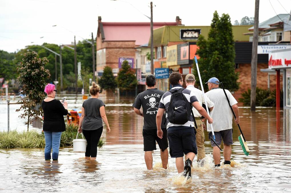 A group of Lismore residents with brooms and cleaning gear wade through the flooded streets. Photo: Kate Geraghty