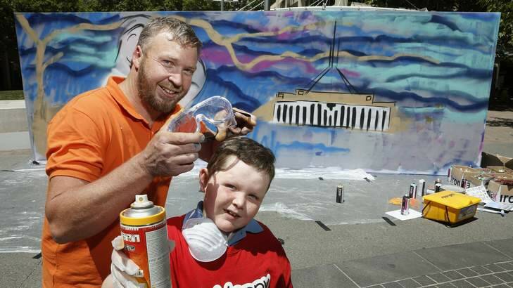 Canberra graffiti artist Geoff Filmer gets Jakub Kowalski, 8, from Fisher ready to lend a hand on the Ronald McDonald House Community Art Wall in City Walk in Civic. Photo: Jeffrey Chan
