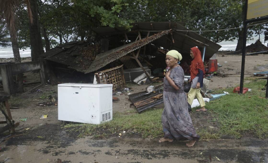 Residents walk past a house damaged by a tsunami, in Carita, Indonesia. Photo: AP