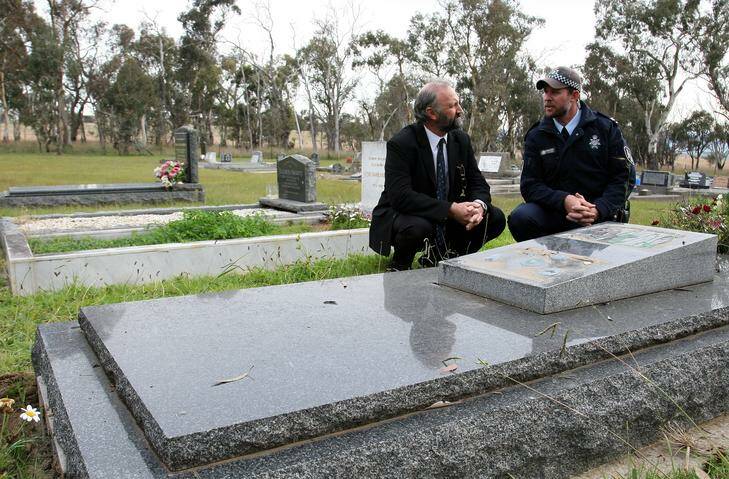 Hamish Horne from the ACT Public Cemetery Authority and Senior Constable Scott Clarke from ACT Policing with one of the damaged graves at Hall General Cemetery.  About 45 plaques have been stolen from the cemetery. Photo: Jeffrey Chan