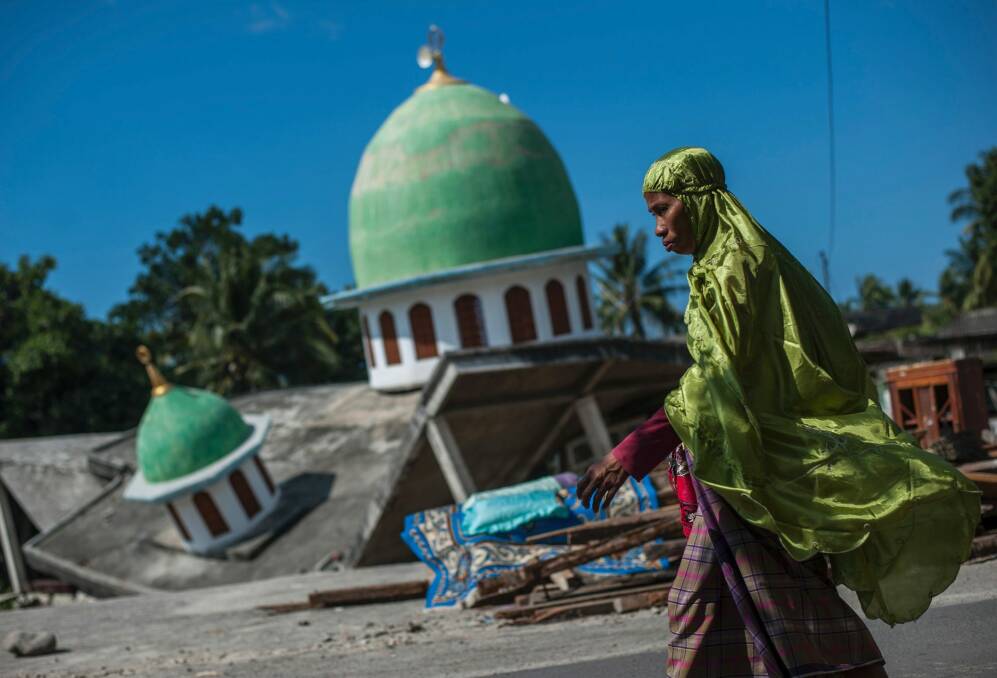 A Muslim woman walks past a mosque collapsed during the August 9 earthquake in Gangga, Lombok Island. Photo: AP