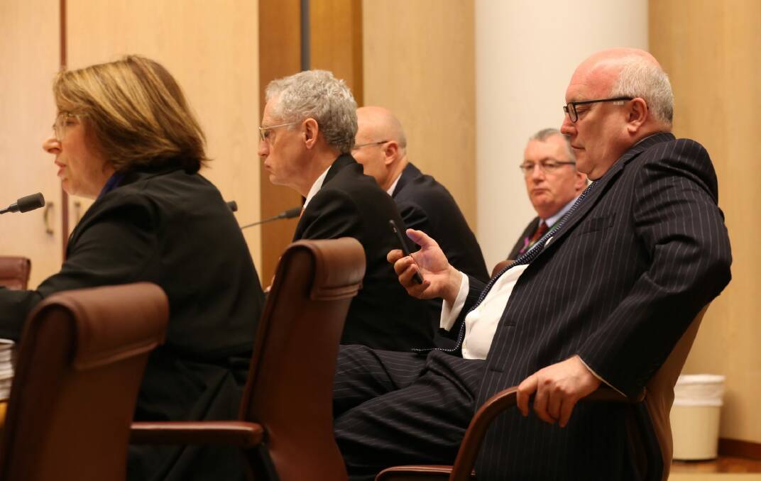 Attorney-General Senator George Brandis (right) checks his phone during the Senate budget estimates hearing with PM&C officials at Parliament House on Monday. Photo: Andrew Meares