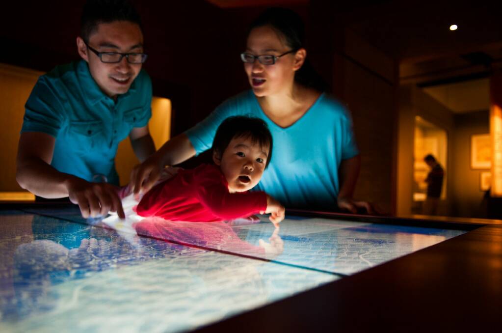 Kevin He with his daughter Cherie and wife Rui Man try out an interactive display at the exhibition. Photo: Elesa Kurtz