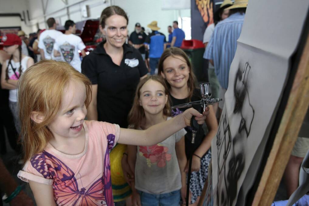 Helen Henry of Darwin, rear, watches as front from left, her daughters Olivia 4, Imogen, 7 and Natasha, 10 try out air brushing at the Anest Iwata stand. Photo: Jeffrey Chan