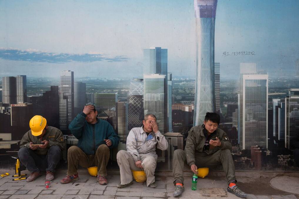 Construction workers rest near a board with an artist's impression of the Central Business District outside a construction site in Beijing. Photo: AP