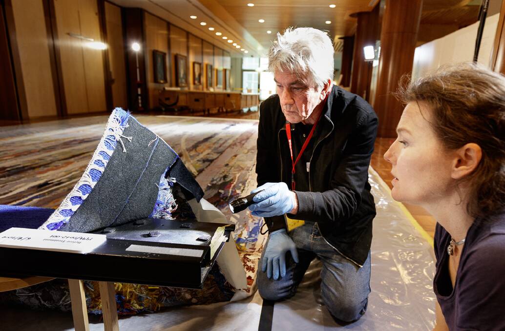 Experts and University of Canberra students toiled for five days to inspect and clean the huge Great Hall tapestry at Parliament House.  Jon Burchill and Lilly Vermeesch inspect the velcro backing. Photo: Parliament House Art Collection