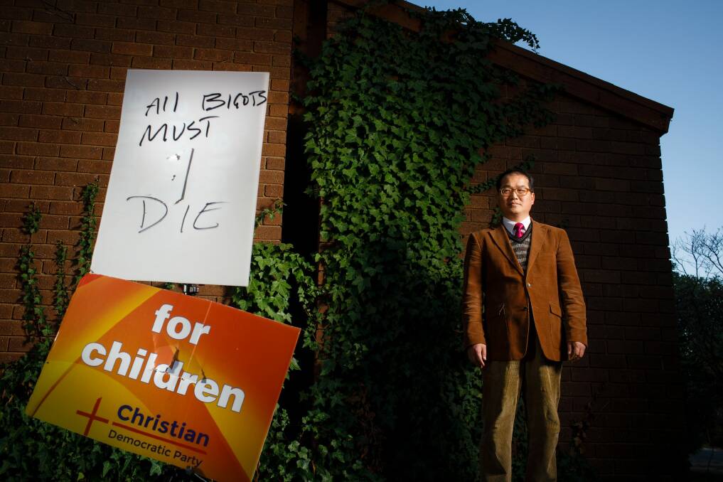 Rev. David Kim with an ACT Christian Democratic Party's anti-safe schools campaign sign which had been torn in half and defaced with an intimidating threat. Photo: Sitthixay Ditthavong