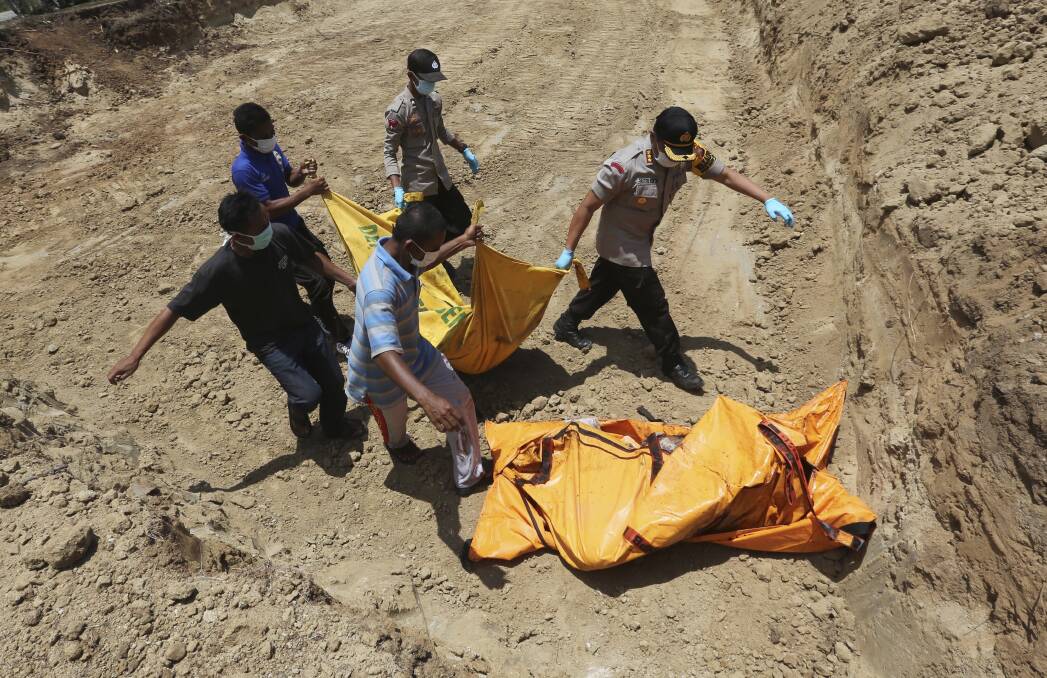 Indonesian rescue team members carry the body of a victim to a grave during a mass burial in Palu on Monday. Photo: AP