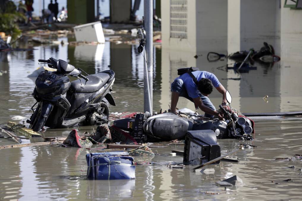 An Indonesian man tries to get his motorbike upright at a tsunami devastated area in Talise beach, Palu. Photo: EPA