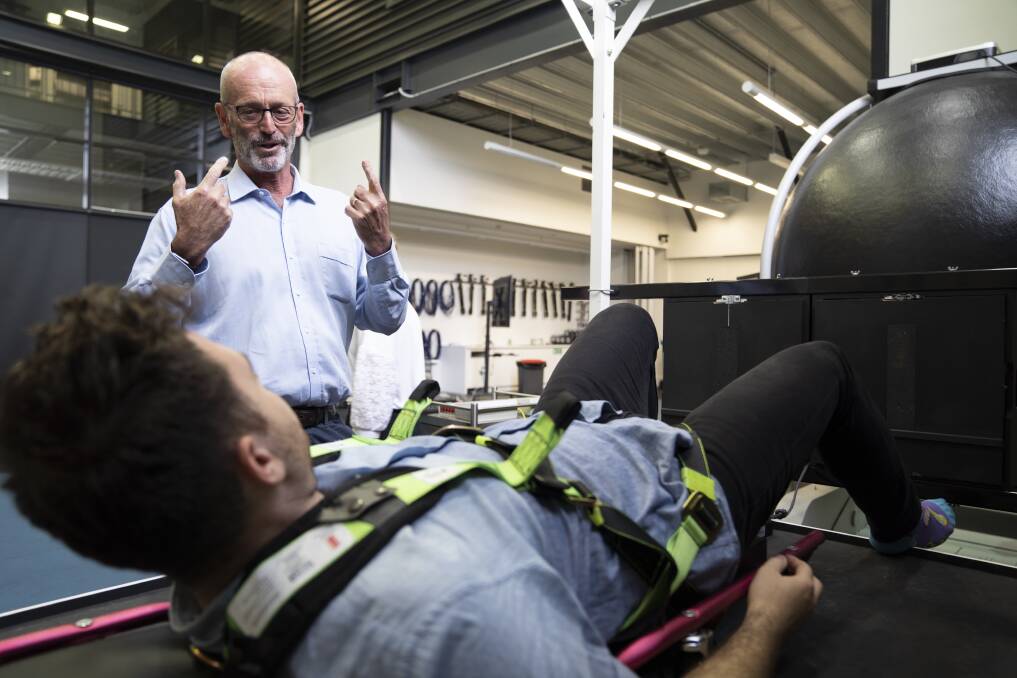 Professor Gordon Waddington explains how the Earth Moon Mars bed works to reporter Elliot Williams. The machine tries to replicate the feeling of different levels of gravity on a person's legs. Photo: Lawrence Atkin