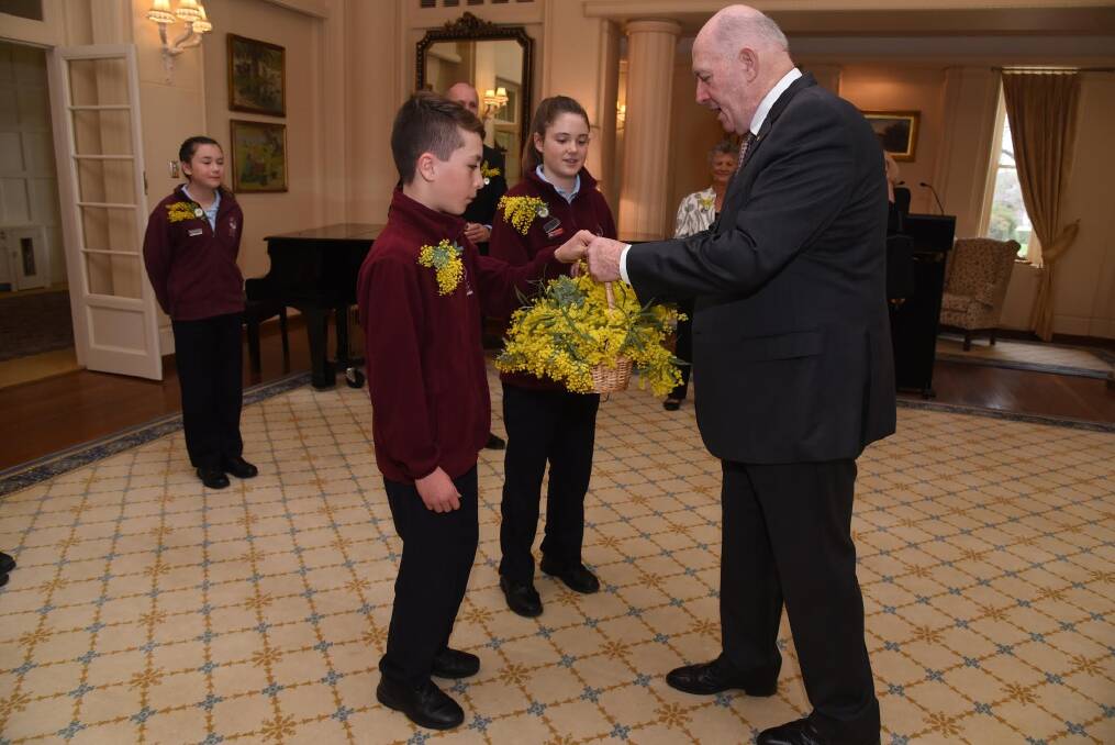 Governor-General Sir Peter Cosgrove receives a basket of wattle from Holy Spirit Primary School Nicholls students Aiden Monteleone and Holly Fahy to mark Wattle Day on Thursday, September 1. Photo: Supplied