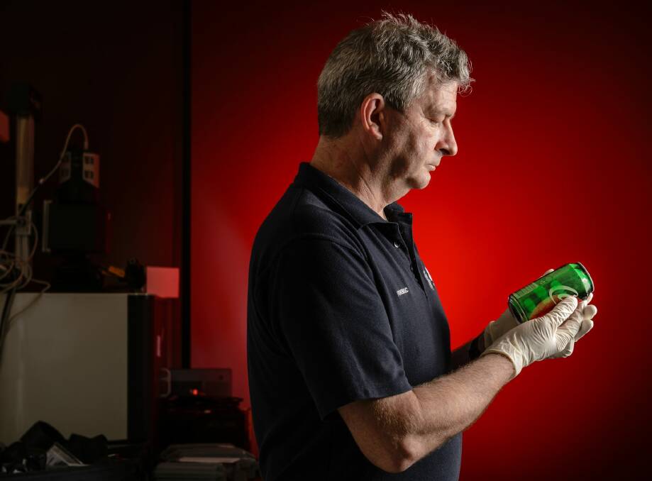 Australian federal police fingerprints expert Phil Herd examines fingerprints on a can of soft drink. Photo: Sitthixay Ditthavong