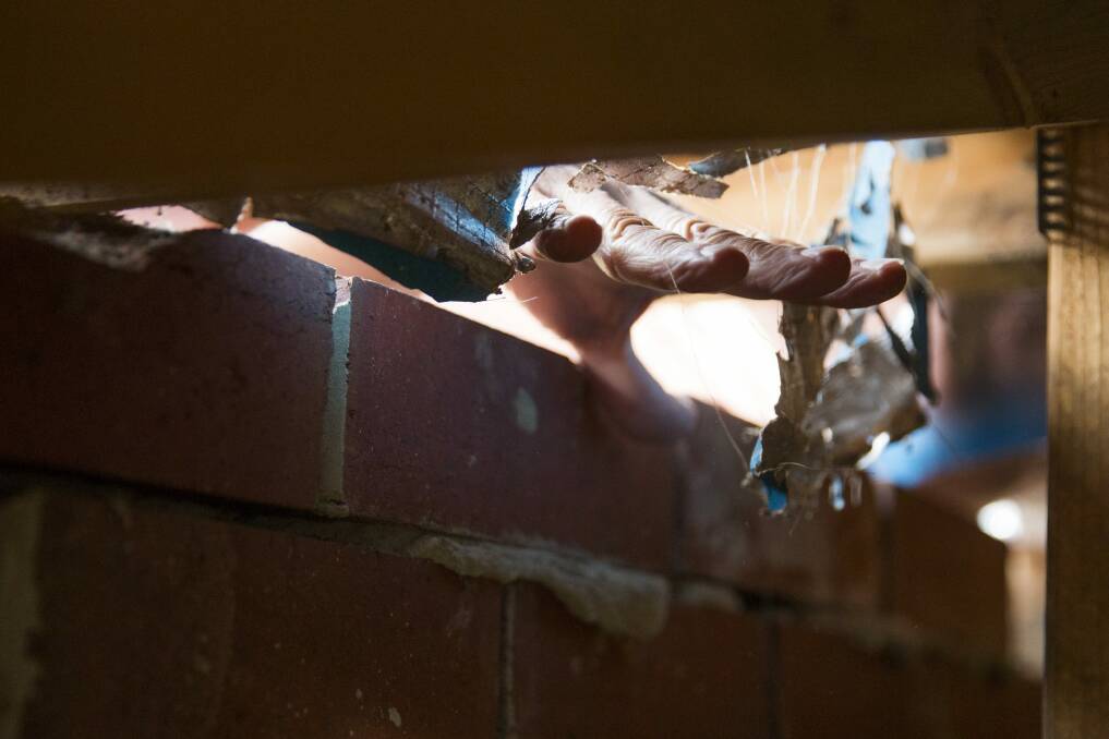 David Merz puts his hand through the gap in his roof where possums have entered after unrepaired damage by Actew AGL. Photo: Matt Bedford