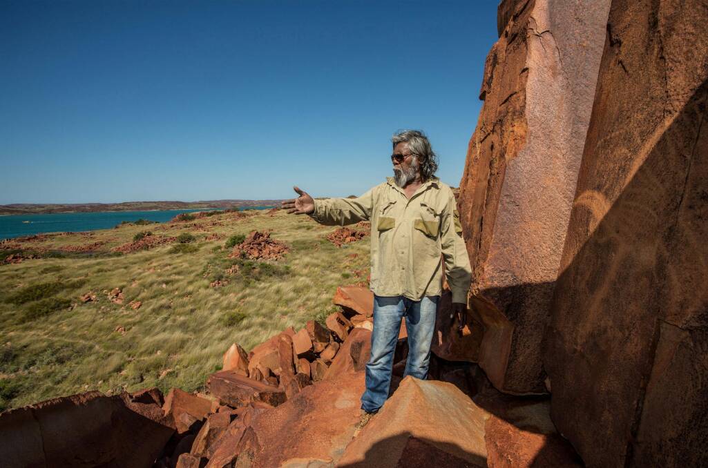 Jakari Togo, a senior cultural ranger at Murujuga National Park, looks out to sea next to rock carvings on the Burrup Peninsula. Photo: Australian Geographic