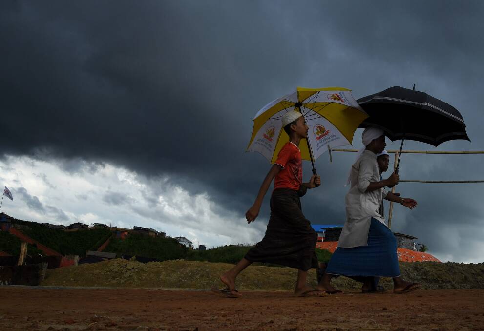 Storm clouds hang overhead as a Rohingya boys carrying umbrellas walk on a main road in Kutupalong camp. Photo: Kate Geraghty