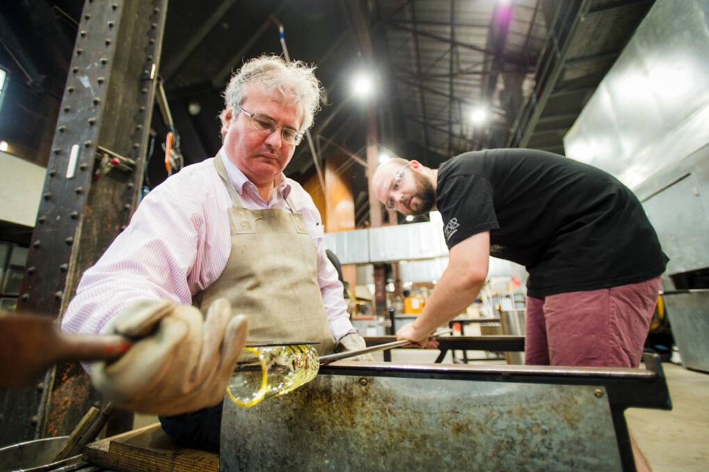 Make Your Own instructor Nick Adams, right, guides <i>Canberra Times</i> reporter Ron Cerabona through the process of making a glass tumbler at Canberra Glassworks. Photo: Sitthixay Ditthavong