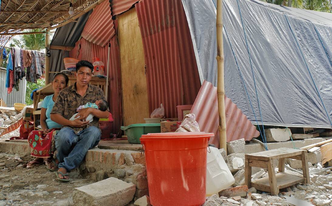 Hanan holds baby Akila, his wife Reniatun behind him, in their makeshift home. Photo: Amilia Rosa