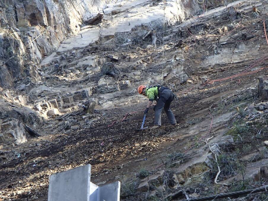 On a slippery slope:  a worker straddles loose rock on a section of Clyde Mountain above the Kings Highway. Photo: Roads and Maritime Services
