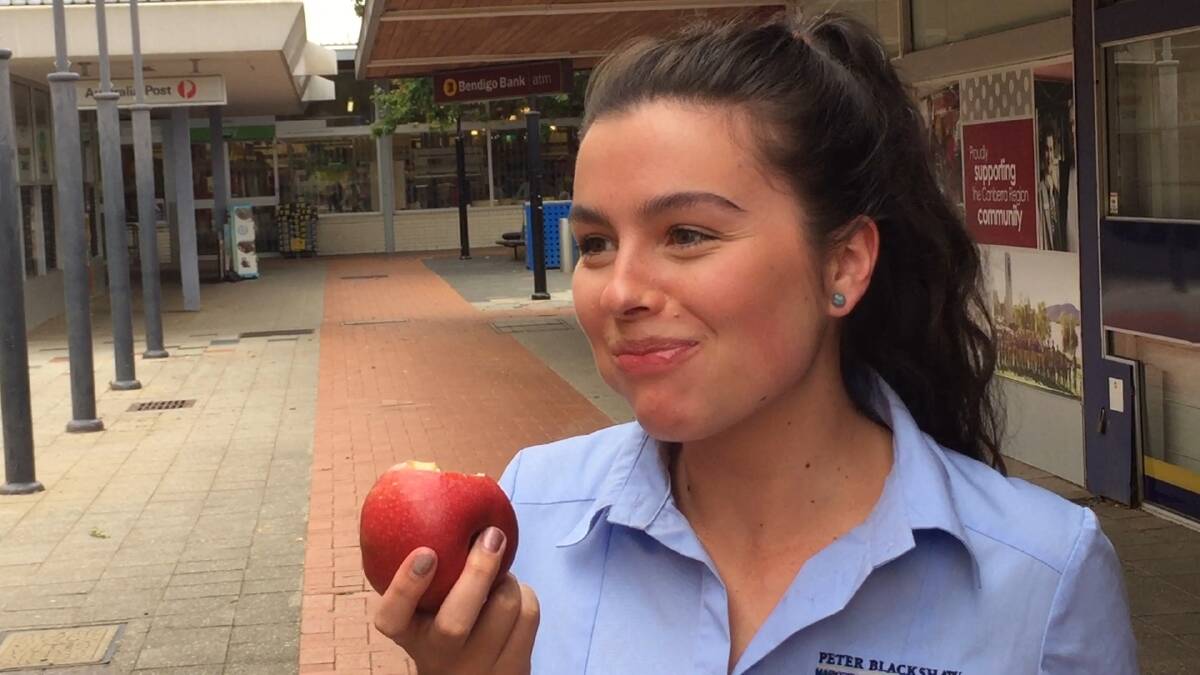 Emily Kelly crunches into a waxless apple outside the Coles store in Curtin.  Photo: Steven Trask