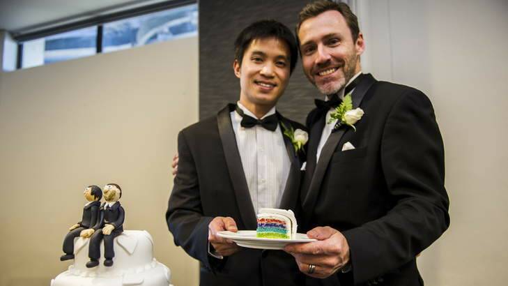 Ivan Hinton and Chris Teoh hold a slice of their rainbow wedding cake at their reception at Telstra Tower. Photo: Rohan Thomson
