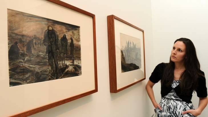 Assistant curator at the Australian War Memorial, Dr. Emma Kindred, with two paintings by WWII official war artist, Alan Moore at an exhibition on show in the WWII galleries. The two images portray activities at the Bergen-Belsen concentration camp, Germany on the day of its liberation. Photo: Graham Tidy GGT