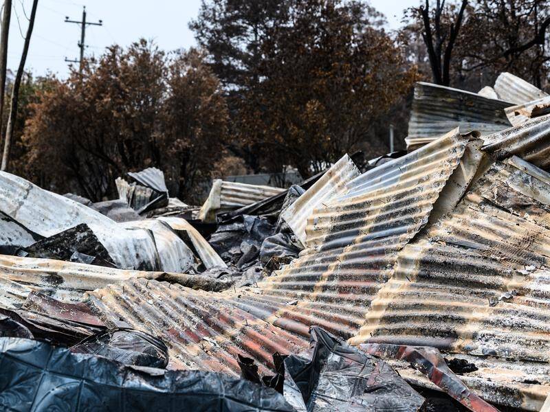 Twisted metal and building debris remains in NSW towns hit by bushfires amid slow clean-up efforts.