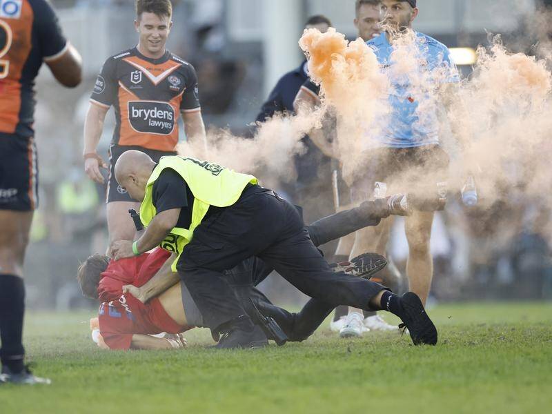 A pitch invader with a flare is tackled by security during a match between Cronulla and Wests.