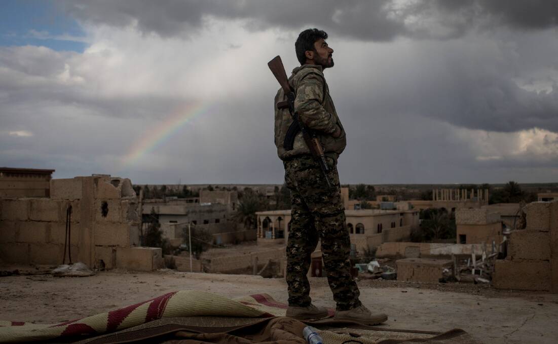 A fighter from the Syrian Democratic Forces, a US-backed Kurdish-led alliance, keeps watch from a rooftop in Bagouz, Syria. Picture: Getty Images