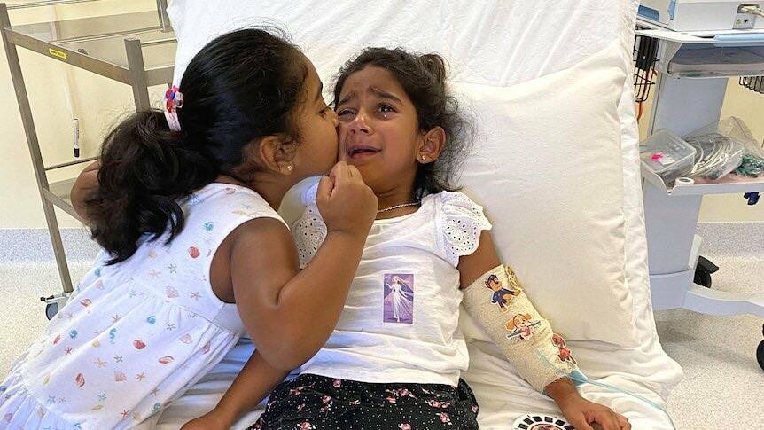 Kopika Murugappan, left, comforts her sister Tharnicaa in hospital on Christmas Island. Picture: Supplied