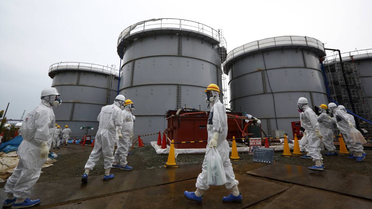 TEPCO employees in protective suits and masks walk past radioactive water storage tanks at the Fukushima Daiichi nuclear power plant. Picture: Getty Images