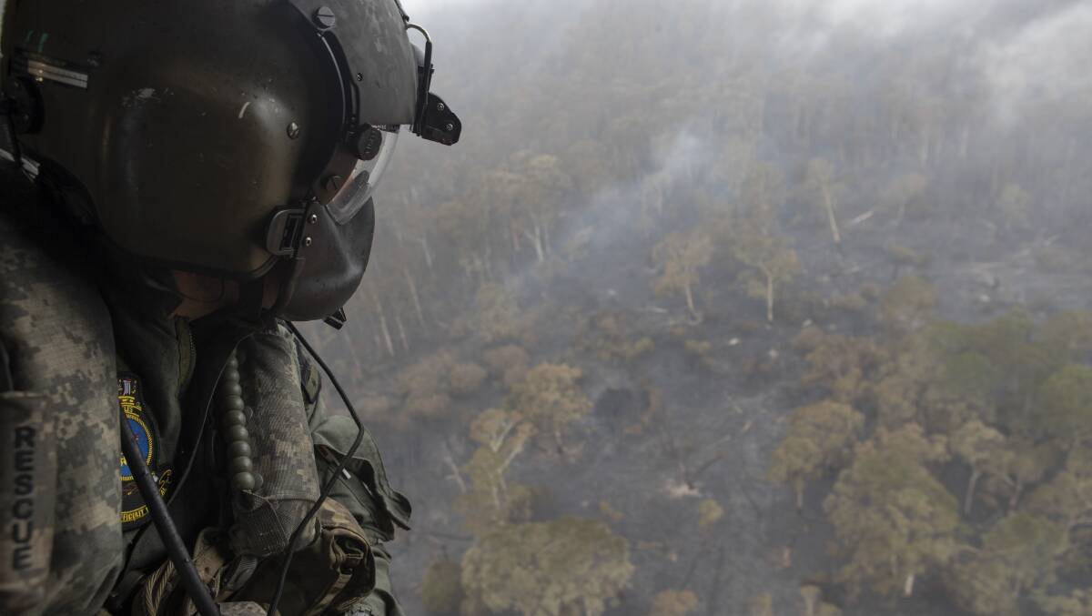 A member of the Defence Force in a maritime support helicopter above burnt land in southern NSW during the Black Summer bushfires. Picture: Department of Defence