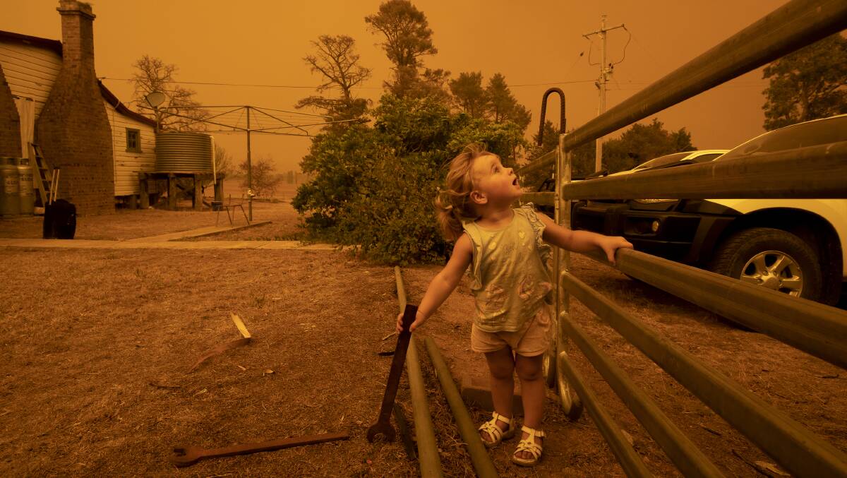 One-year-old Chelsea Povey watches the sky darken over her family property in Colinton due to the Clear Ridge bushfire. Picture: Sitthixay Ditthavong