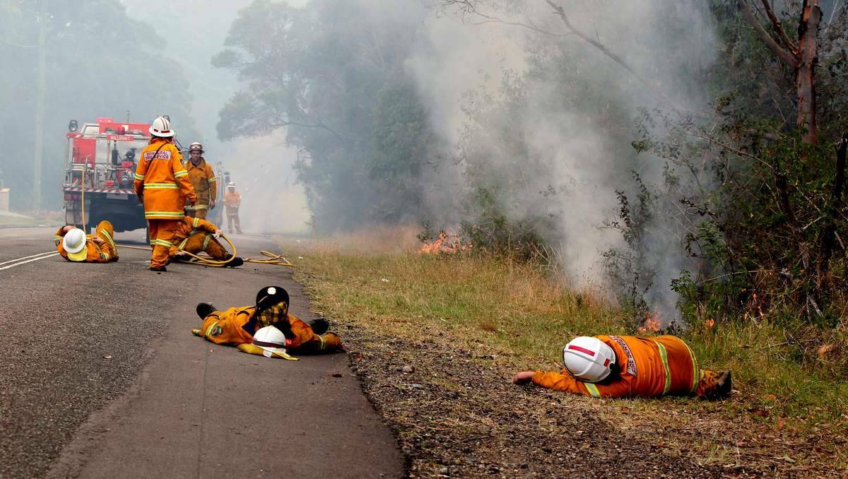 Exhausted firefighters take a rest while fire burns beside them in Cragan Bay Road, Nords Wharf. Photo by PHIL HEARNE, Newcastle Herald.
